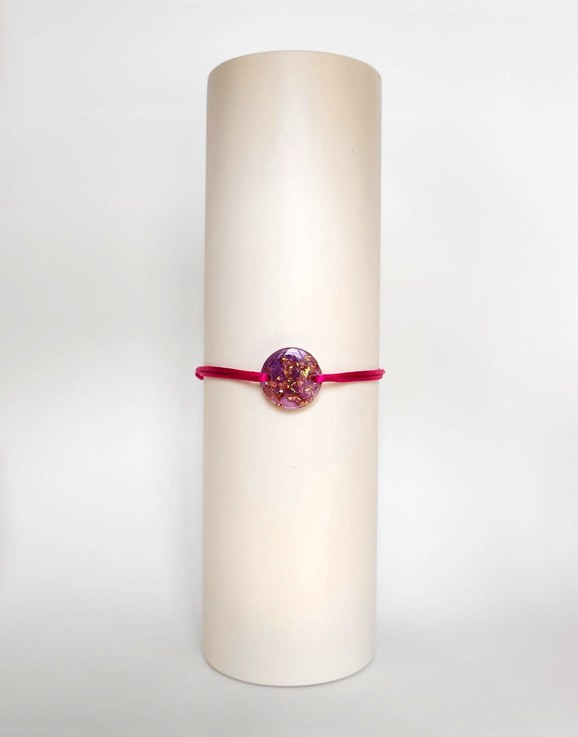 Image d'un modèle de bracelet Mimi avec son cordon satiné de couleur fushia et sa pastille ronde en résine incrustée de poudre de mica rose et de paillettes de feuille de cuivre dorée.