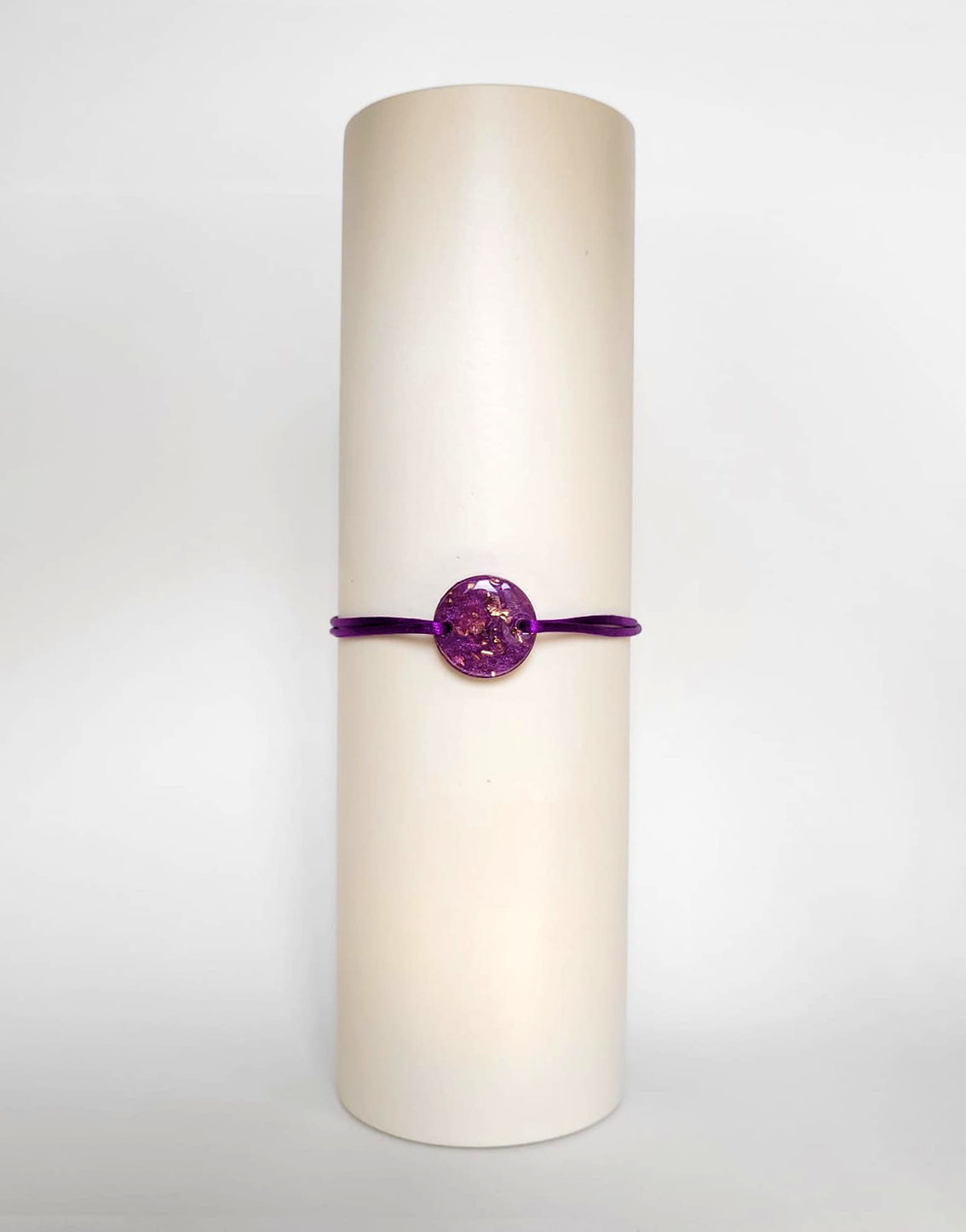 Image d'un modèle de bracelet Mimi avec son cordon satiné de couleur violette et sa pastille ronde en résine incrustée de poudre de mica rose et de paillettes de feuille de cuivre dorée.