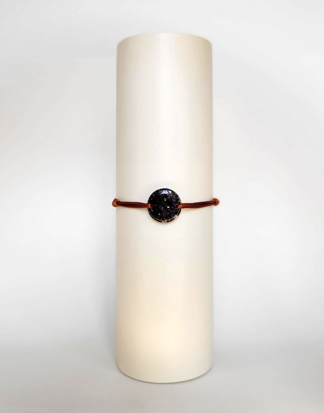 Image d'un modèle de bracelet Mimi avec son cordon satiné de couleur cuivrée et sa pastille ronde en résine incrustée de fleurs naturelles séchées noires et de paillettes de feuille de cuivre dorée.