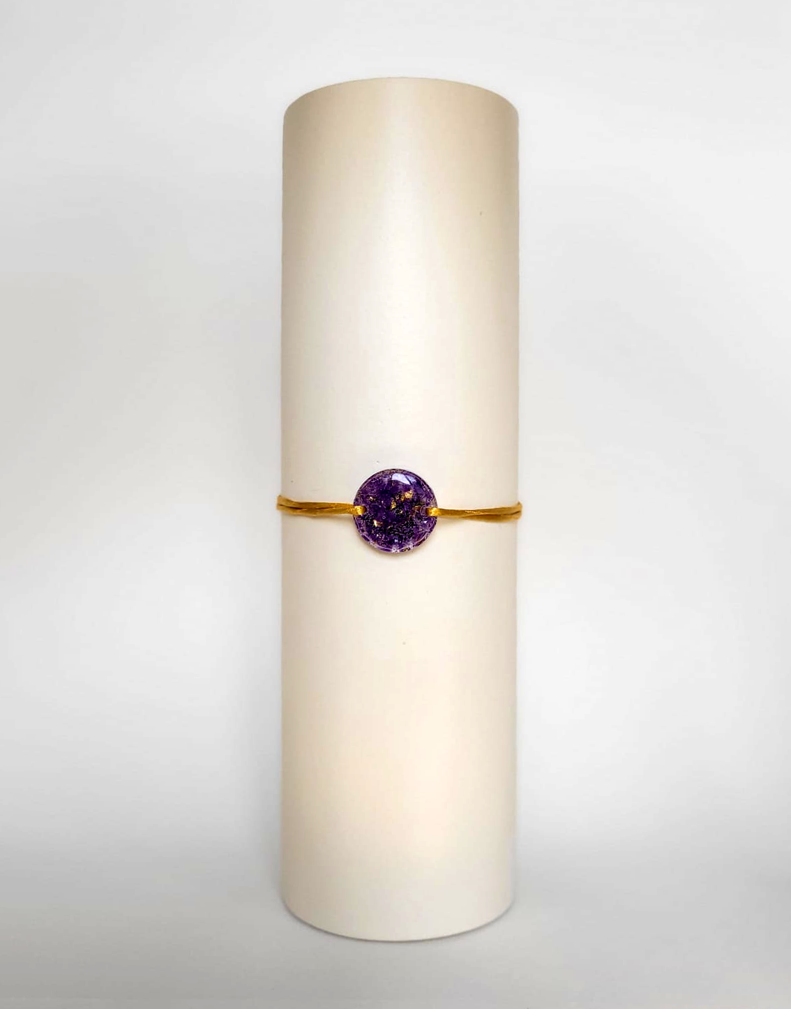 Image d'un modèle de bracelet Mimi avec son cordon satiné de couleur jaune et sa pastille ronde en résine incrustée de fleurs naturelles séchées violettes et de paillettes de feuille de cuivre dorée.