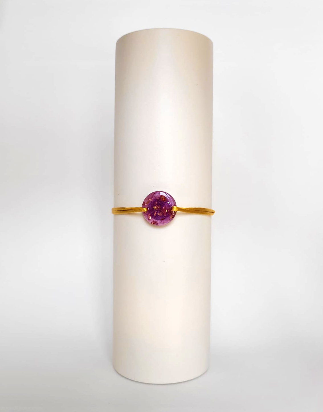 Image d'un modèle de bracelet Mimi avec son cordon satiné de couleur jaune et sa pastille ronde en résine incrustée de poudre de mica rose et de paillettes de feuille de cuivre dorée.