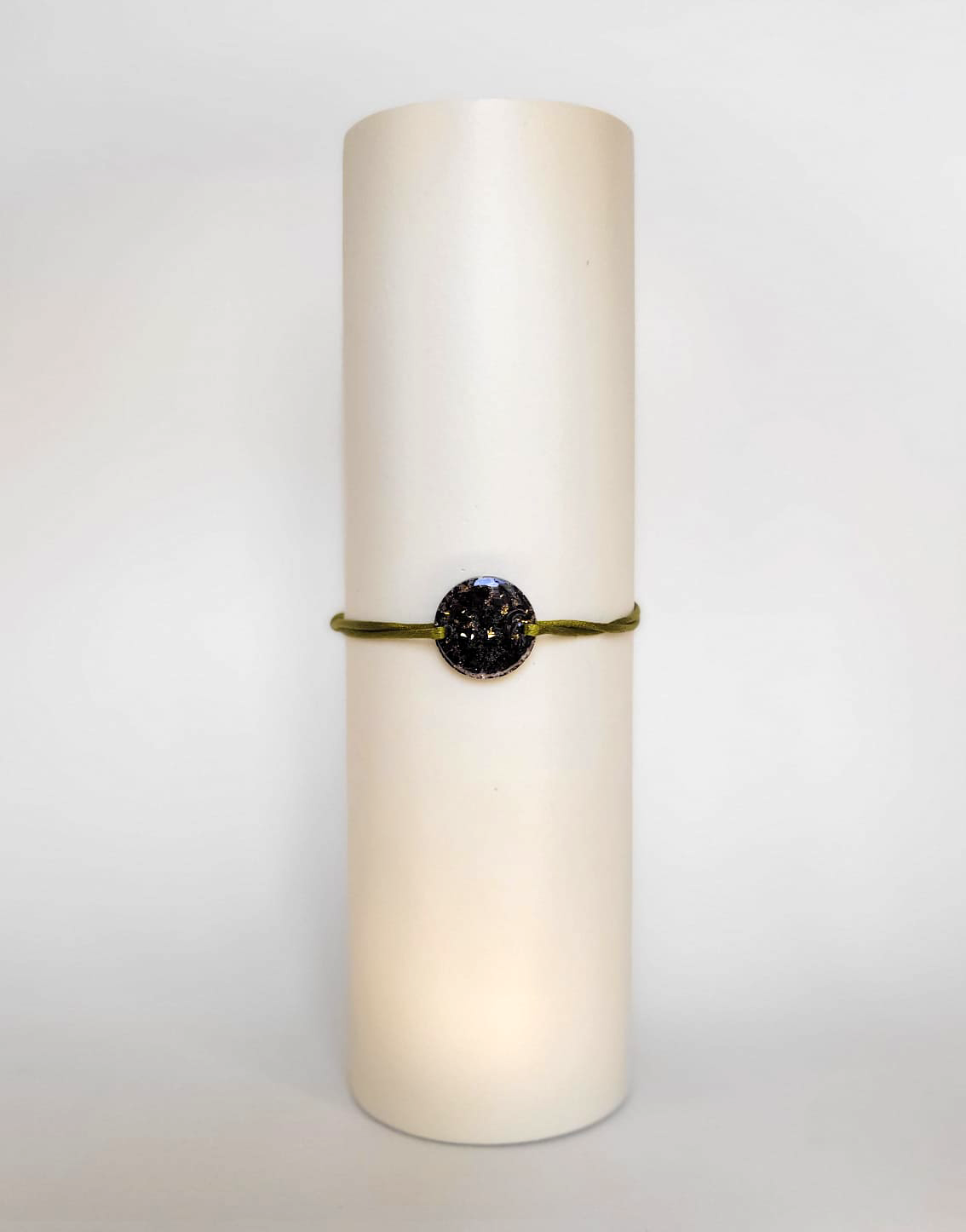 Image d'un modèle de bracelet Mimi avec son cordon satiné de couleur kakie et sa pastille ronde en résine incrustée de fleurs naturelles séchées noires et de paillettes de feuille de cuivre dorée.