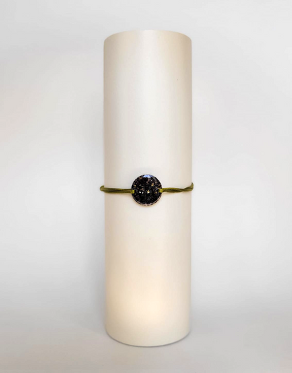 Image d'un modèle de bracelet Mimi avec son cordon satiné de couleur kakie et sa pastille ronde en résine incrustée de fleurs naturelles séchées noires et de paillettes de feuille de cuivre dorée.
