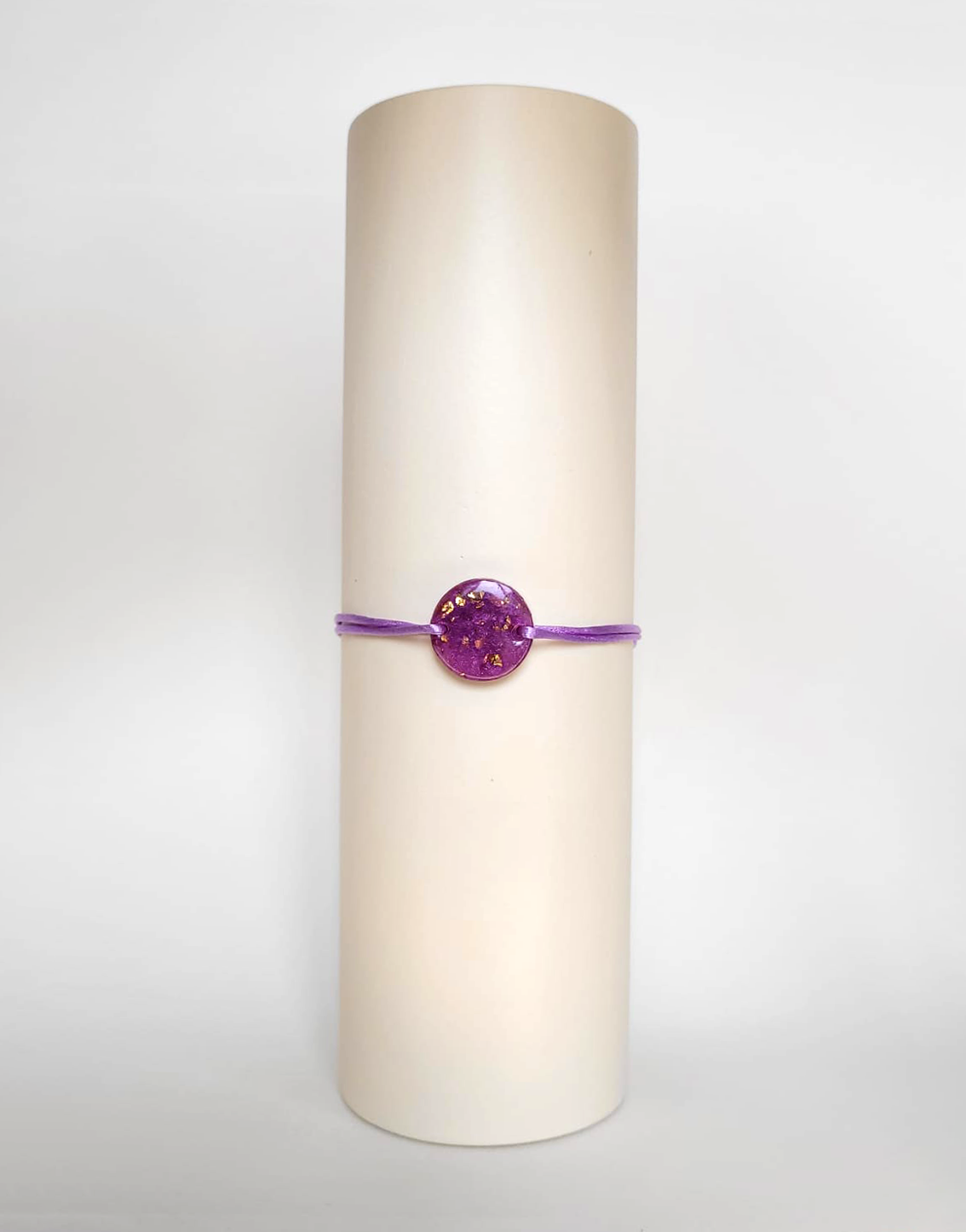 Image d'un modèle de bracelet Mimi avec son cordon satiné de couleur lilas et sa pastille ronde en résine incrustée de poudre de mica rose et de paillettes de feuille de cuivre dorée.
