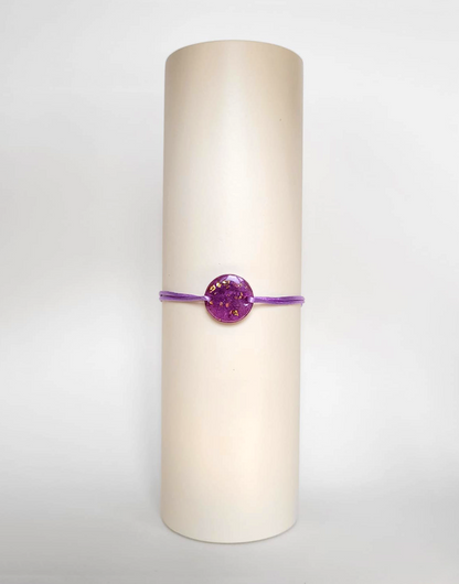 Image d'un modèle de bracelet Mimi avec son cordon satiné de couleur lilas et sa pastille ronde en résine incrustée de poudre de mica rose et de paillettes de feuille de cuivre dorée.