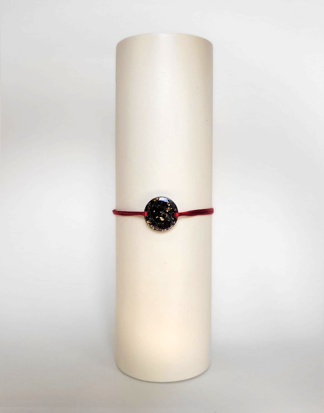 Image d'un modèle de bracelet Mimi avec son cordon satiné de couleur rouge et sa pastille ronde en résine incrustée de fleurs naturelles séchées noires et de paillettes de feuille de cuivre dorée.