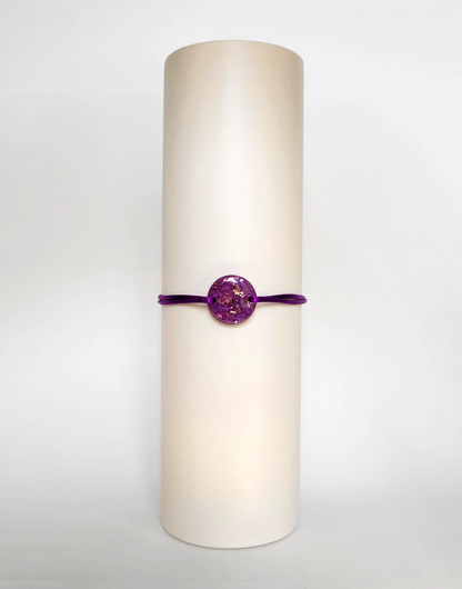 Image d'un modèle de bracelet Mimi avec son cordon satiné de couleur violette et sa pastille ronde en résine incrustée de poudre de mica rose et de paillettes de feuille de cuivre dorée.